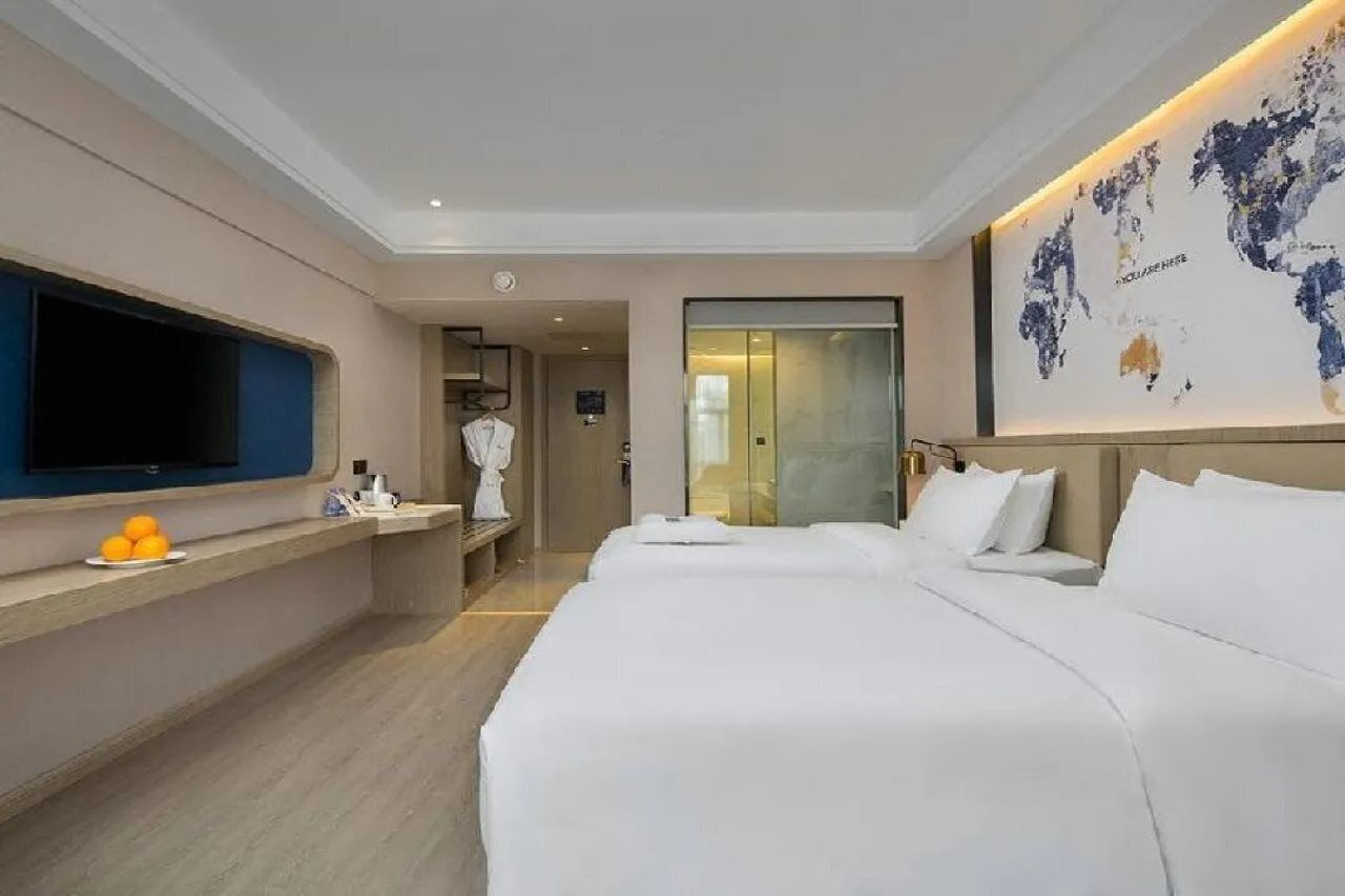 Une chambre d’hôtel avec deux lits, un téléviseur à écran plat, une petite table avec des oranges et une carte du monde accrochée au mur.
