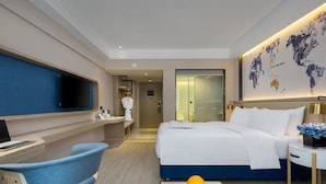 A modern hotel room with a bed, a desk with a computer, a chair, and a wall-mounted TV.