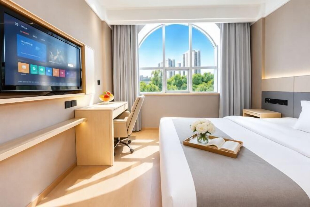 Habitación de hotel con una cama grande, un escritorio, un televisor y una ventana con vista a la ciudad.