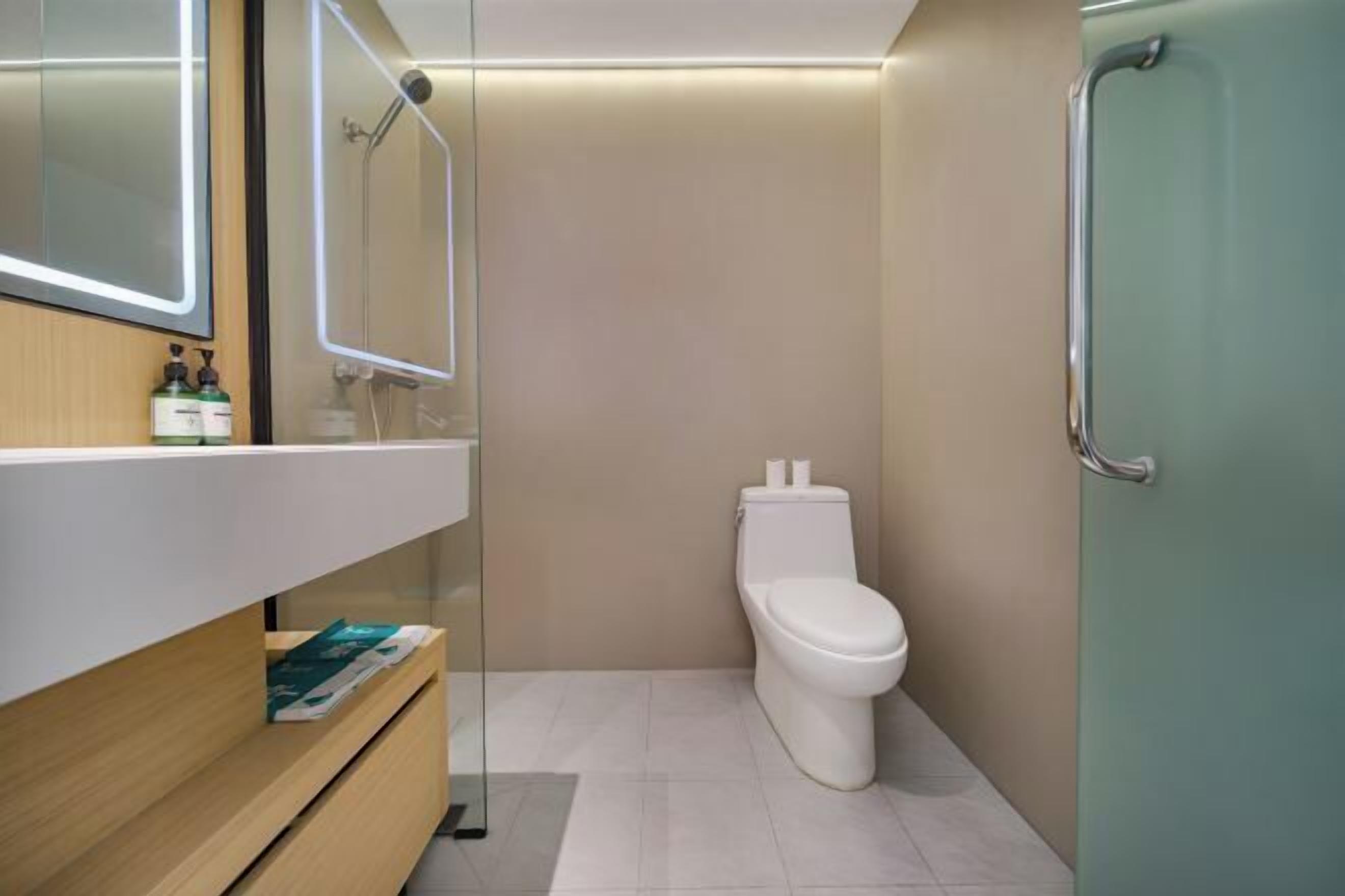 A modern bathroom with a toilet, a glass-enclosed vanity, and a shower area.
