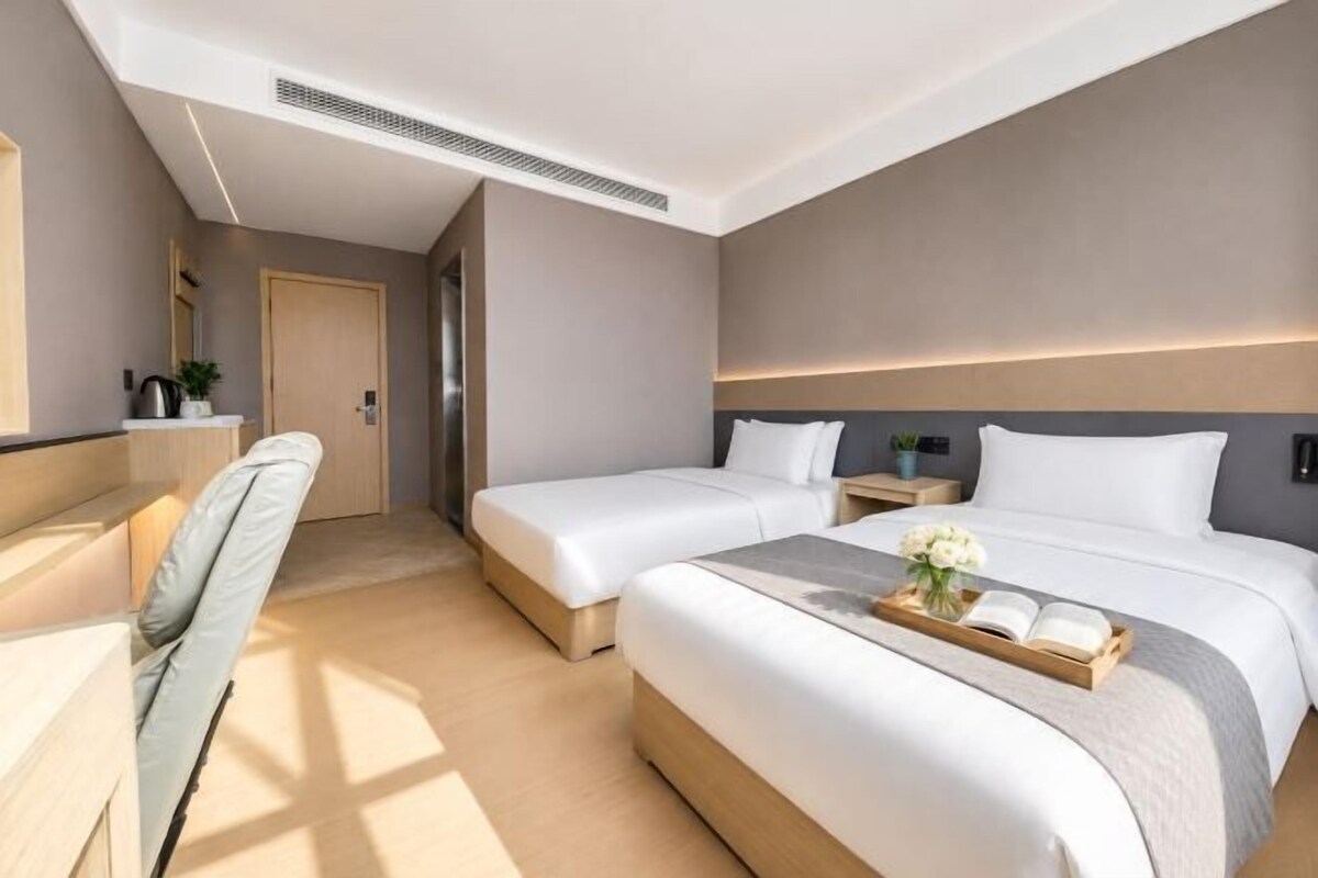 Habitación de hotel con dos camas, un escritorio, una silla y una mesita con un florero.