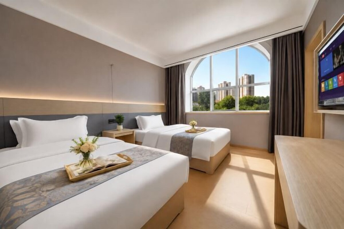 Habitación de hotel con dos camas, un escritorio, un ventanal con vista a la ciudad y un televisor.