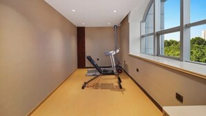 A gym with exercise equipment, a window with a view, and a wooden floor. - Urban Garden Hotel (Qingdao)
