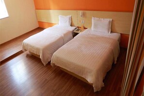 Habitación de hotel con dos camas, piso de madera y una pared de acento naranja.