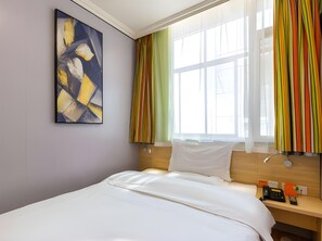 Habitación de hotel con cama, mesita de noche con lámpara, un cuadro en la pared y ventana con cortinas.