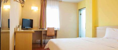 A hotel room with a bed, a desk with a chair, a television, and a window with curtains.