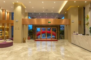 Un vestíbulo de hotel con piso de mármol, una recepción y una entrada de vidrio con un detalle decorativo rojo en el exterior.
