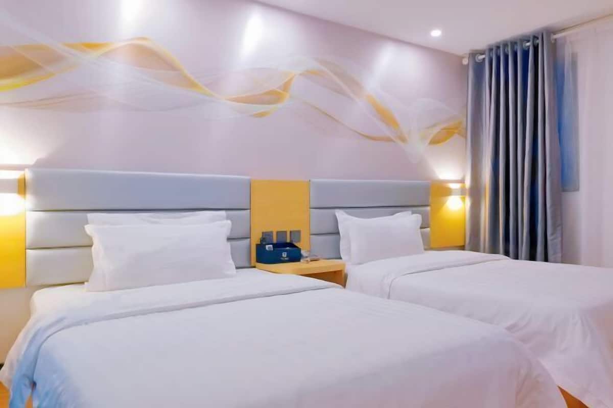 A hotel room with two beds, a headboard, bedside tables, and a wall with abstract art.