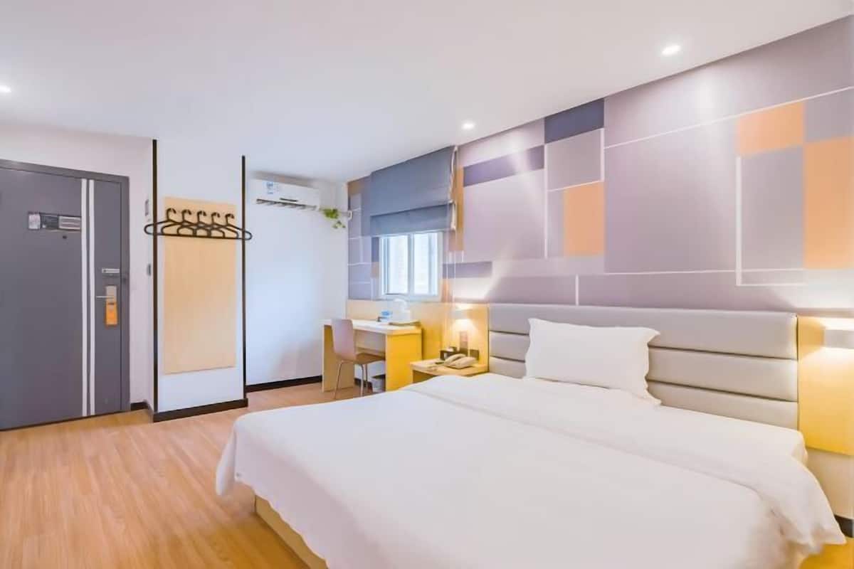 A hotel room with a bed, a desk, a chair, a wardrobe, and a wall-mounted coat rack.