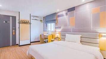 A hotel room with a bed, a desk, a chair, a wardrobe, and a wall-mounted coat rack.