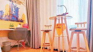 A hotel room with a wooden floor, a desk with a chair, a round table with a heart-shaped sign, and a cat bed. - 7Days Inn Hotel (Huizhou Zhongkai Chenjiang Avenue) (Huizhou)