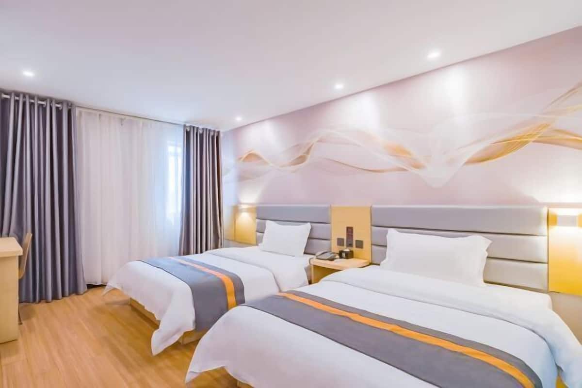 A hotel room with two beds, a wooden floor, a large window with curtains, and a modern wall design.