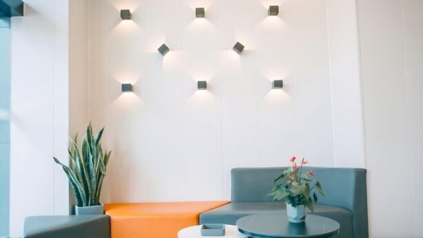 A modern waiting area with a grey sofa, orange bench, and a small round table with a vase of flowers. - 7Days Inn Hotel (Huizhou Zhongkai Chenjiang Avenue) (Huizhou)