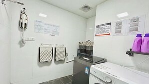 A laundry room with a washing machine, a dryer, and a telephone. There are towels hanging on hooks and a shelf with laundry supplies. - 7Days Inn Hotel (Huizhou Zhongkai Chenjiang Avenue) (Huizhou)