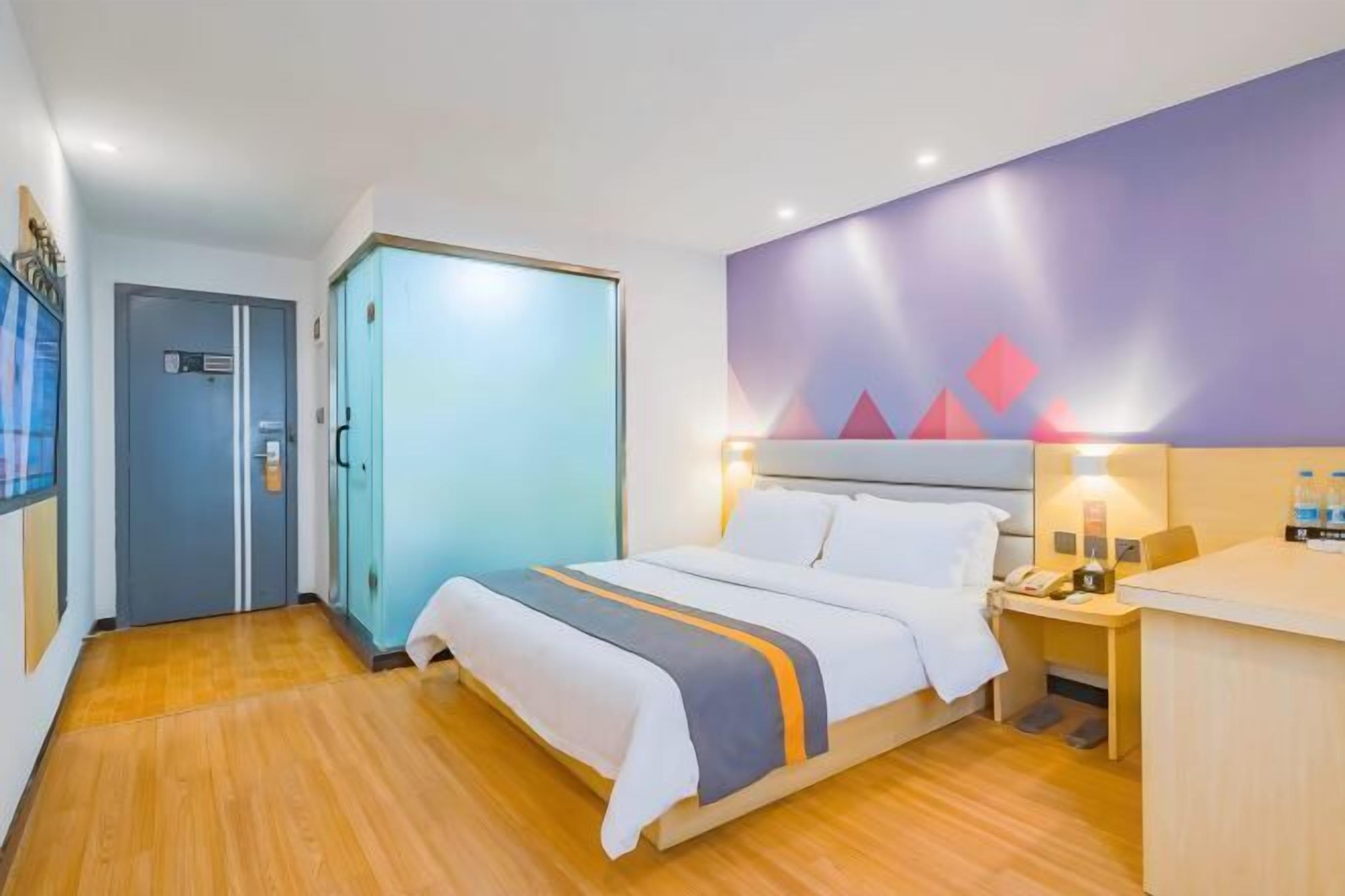 A hotel room with a bed, bedside table, and a desk with a chair.