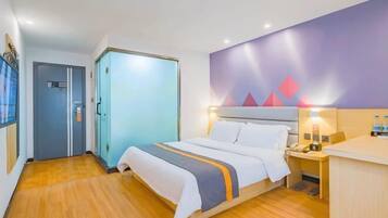 A hotel room with a bed, bedside table, and a desk with a chair.