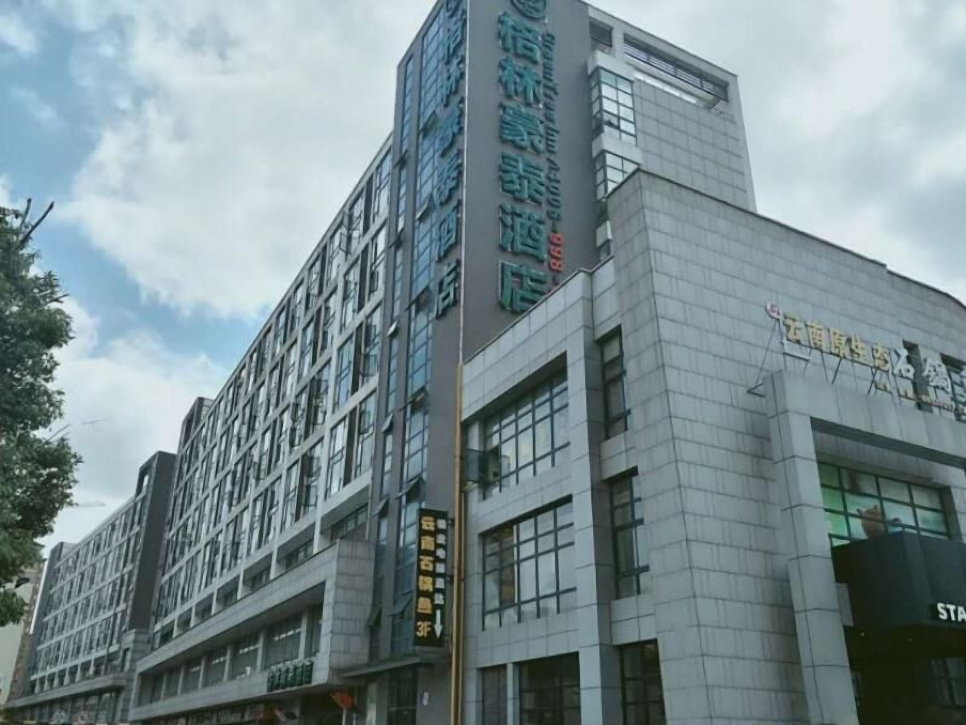 A multi-story hotel with a modern architectural design, featuring a prominent vertical sign with text, large windows, and a flat roof.