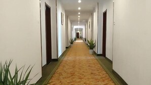 Un largo pasillo de hotel estrecho, con suelo alfombrado, paredes blancas y puertas a ambos lados.