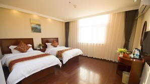 Habitación de hotel con dos camas, un escritorio con televisor y un ventanal con cortinas.