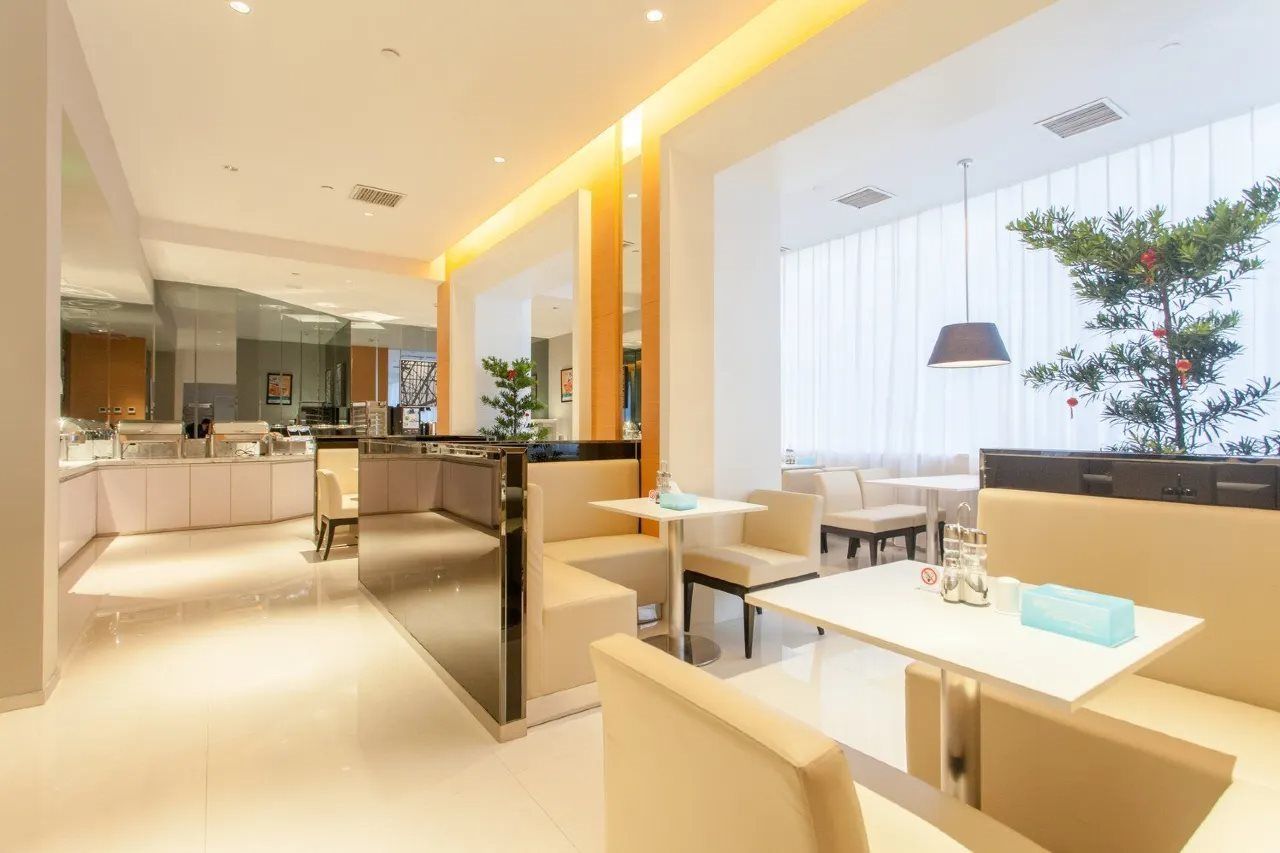 A modern hotel lobby with a kitchen area, seating arrangements, and a large window with a view.