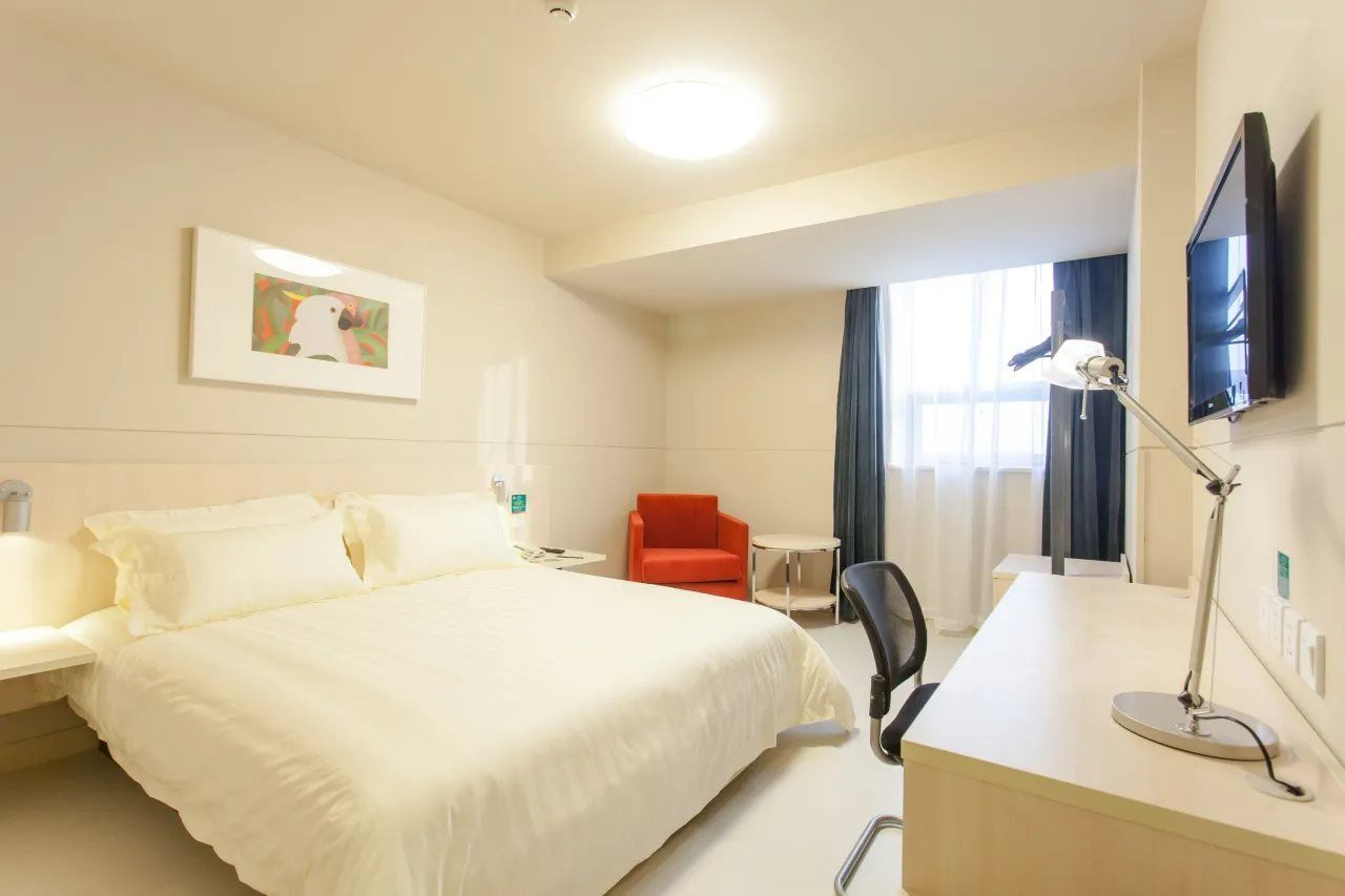 A hotel room with a bed, a desk, a chair, a TV, and a painting on the wall.