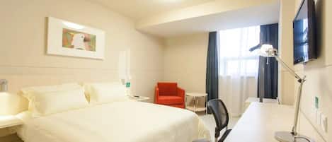 Quarto de hotel com cama, escrivaninha, cadeira, televisão e um quadro na parede.