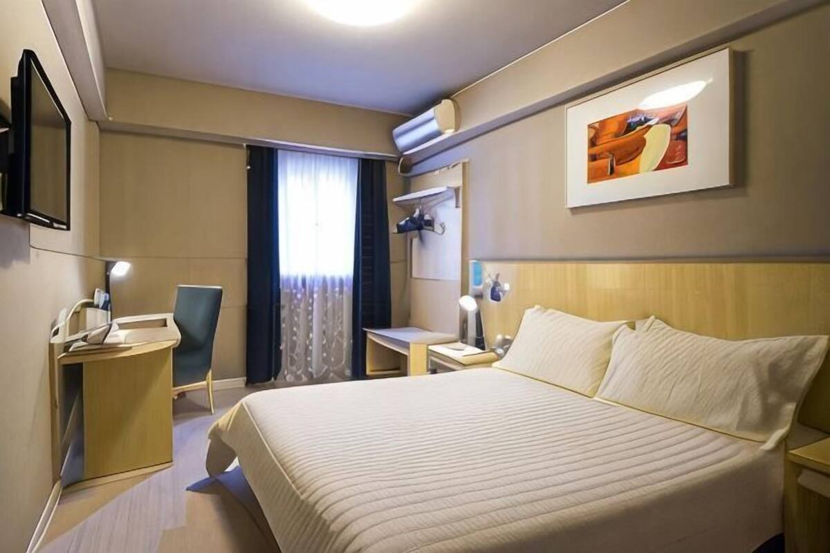 A hotel room with a bed, a desk, a chair, a TV, and a window with curtains.