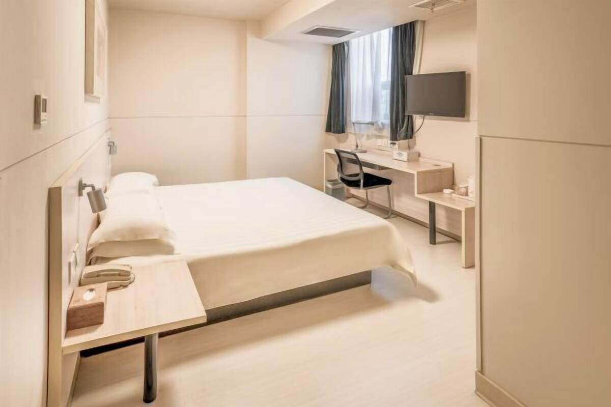 A hotel room with a bed, a desk, a chair, a TV, and a window with curtains.
