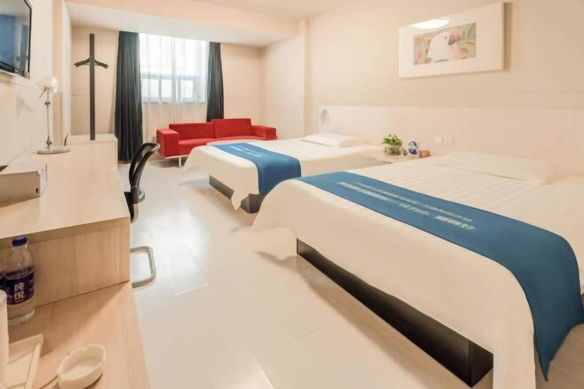 A hotel room with two beds, a desk with a lamp, a chair, a TV, and a window with curtains.
