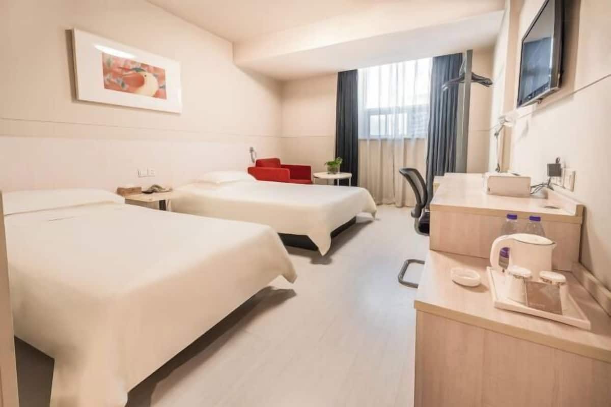 A hotel room with two beds, a desk with a coffee maker, and a TV on the wall.