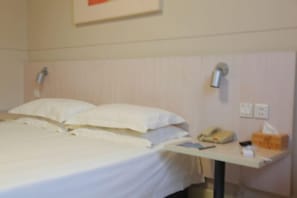 Quarto de hotel com cama, mesa de cabeceira com abajur, telefone e caixa de lenços.