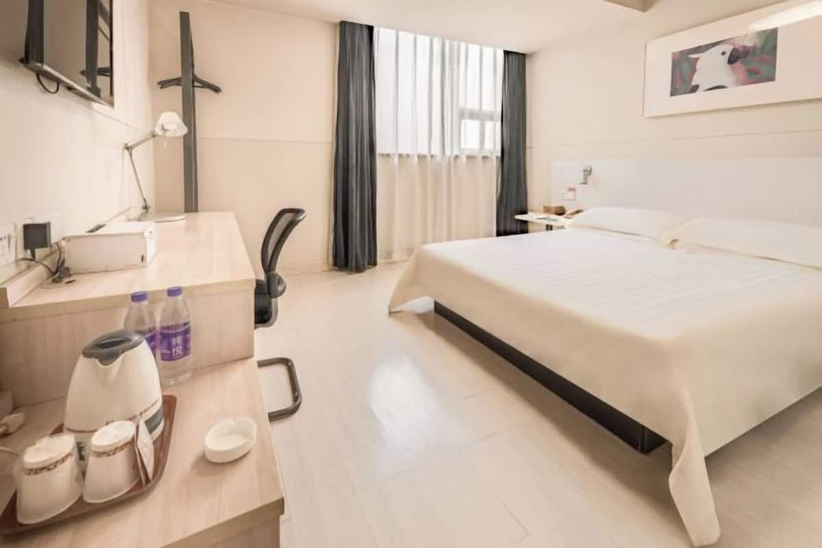 A hotel room with a bed, desk, chair, and a window with curtains.