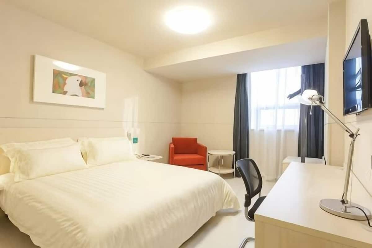 A hotel room with a bed, a desk, a chair, a TV, and a window with curtains.