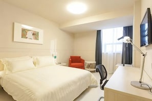 A hotel room with a bed, a desk, a chair, a TV, and a window with curtains.