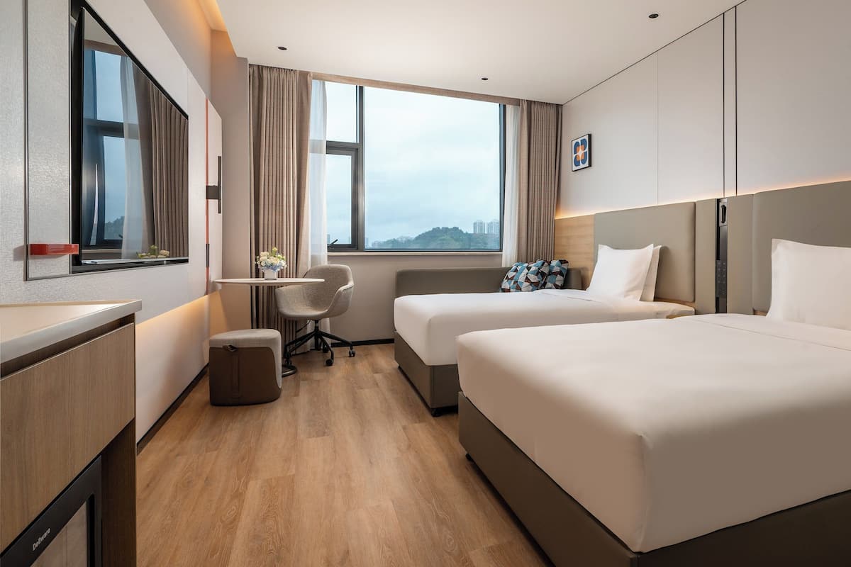 Une chambre d’hôtel avec deux lits, un bureau, une chaise et une vue sur la ville.
