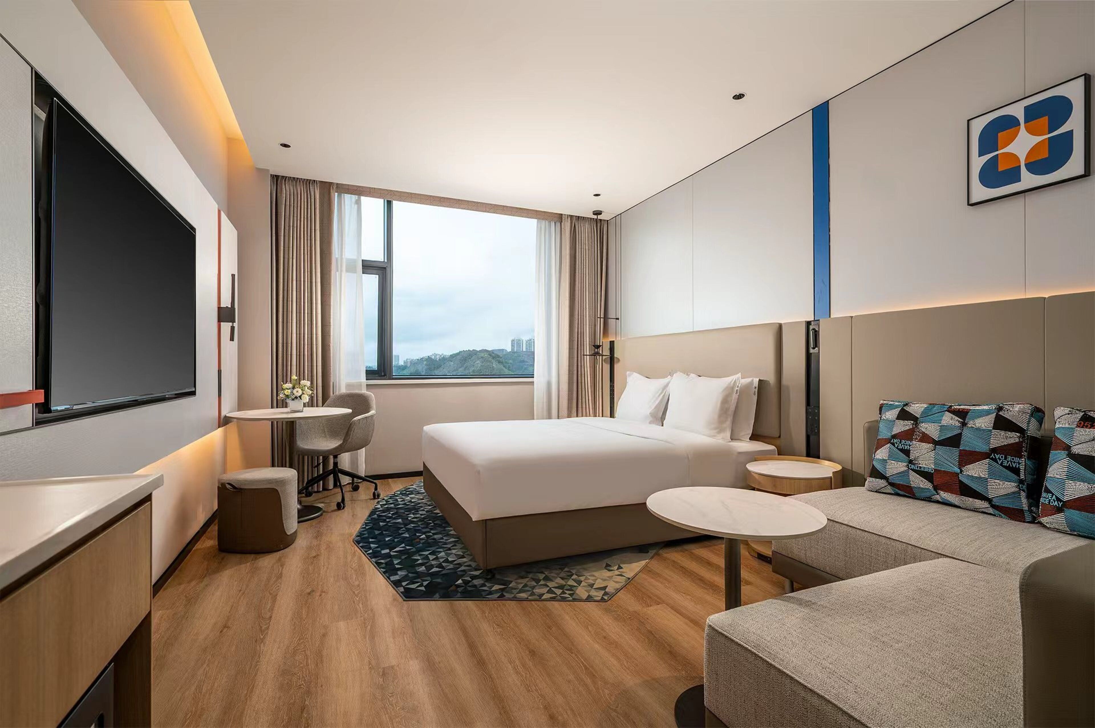 Una habitación de hotel moderna con una cama grande, un sofá, un escritorio y un televisor.