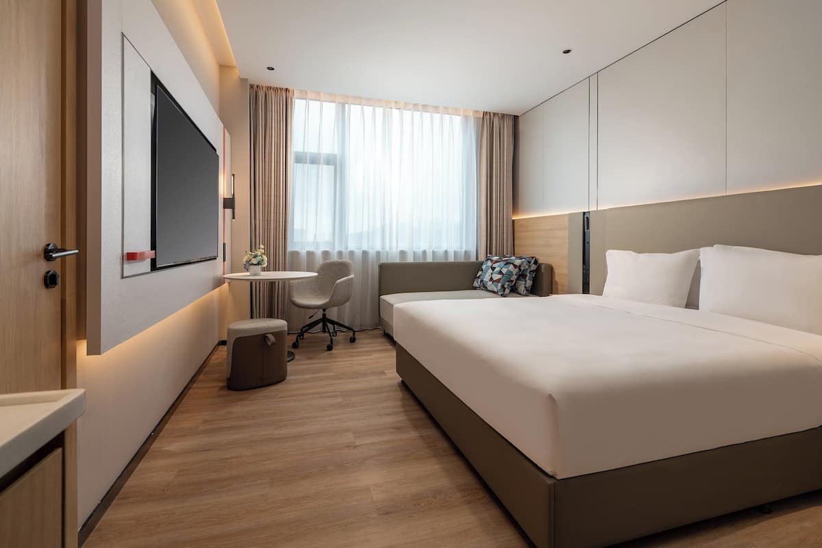 Une chambre d’hôtel moderne équipée d’un grand lit, d’un bureau, d’une chaise et d’un téléviseur fixé au mur.