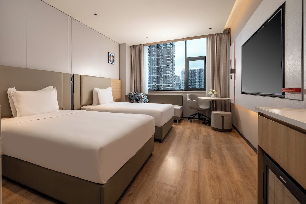 Une chambre d’hôtel avec deux lits, un bureau, une chaise, une télévision et une fenêtre donnant sur la ville.