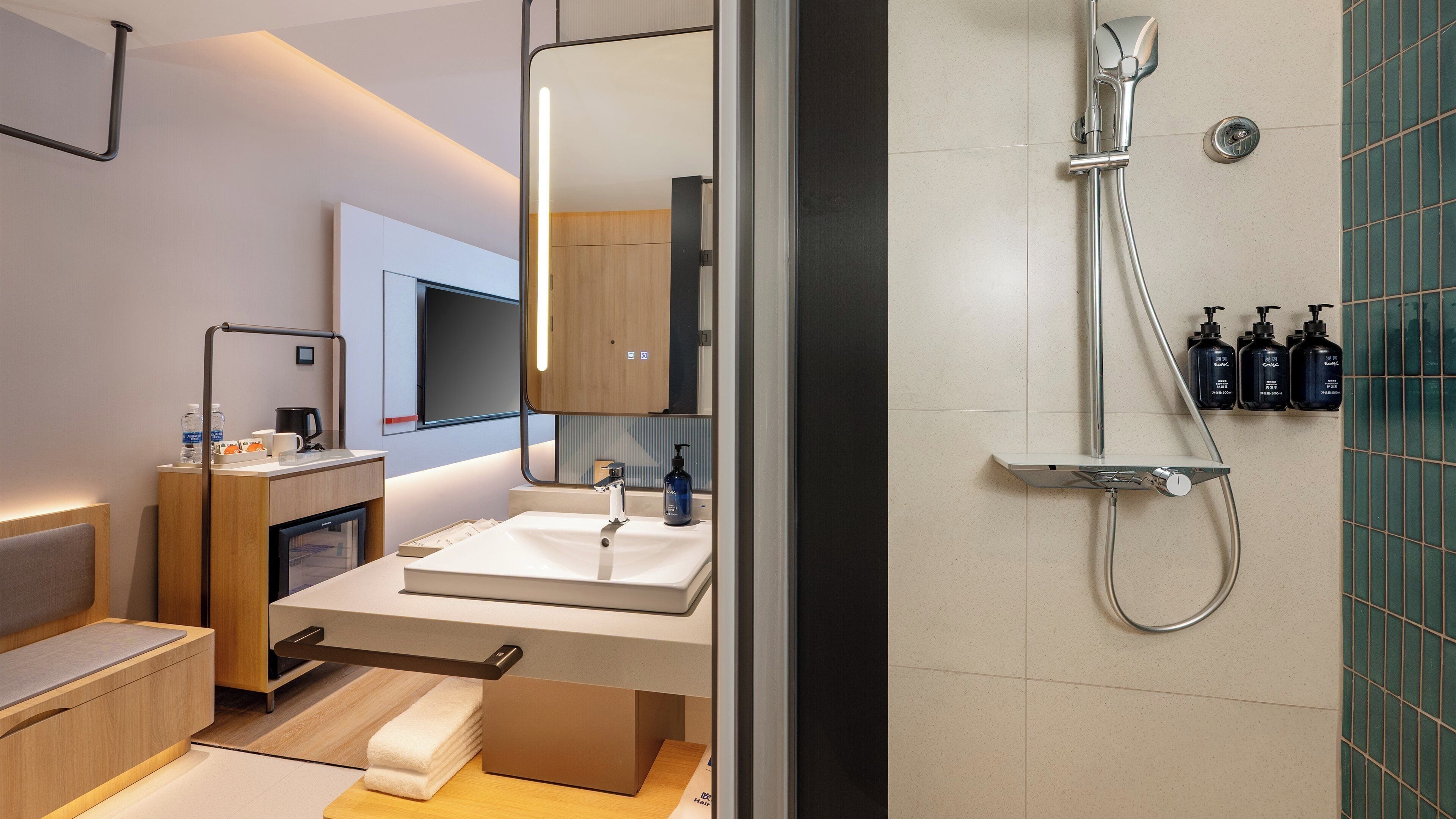 Un baño moderno con lavamanos, espejo y ducha. Hay artículos de aseo en la encimera y un perchero para toallas.