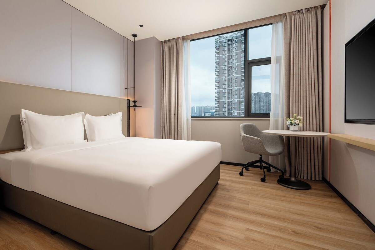 Une chambre d’hôtel avec un grand lit, un bureau, une chaise et un téléviseur.