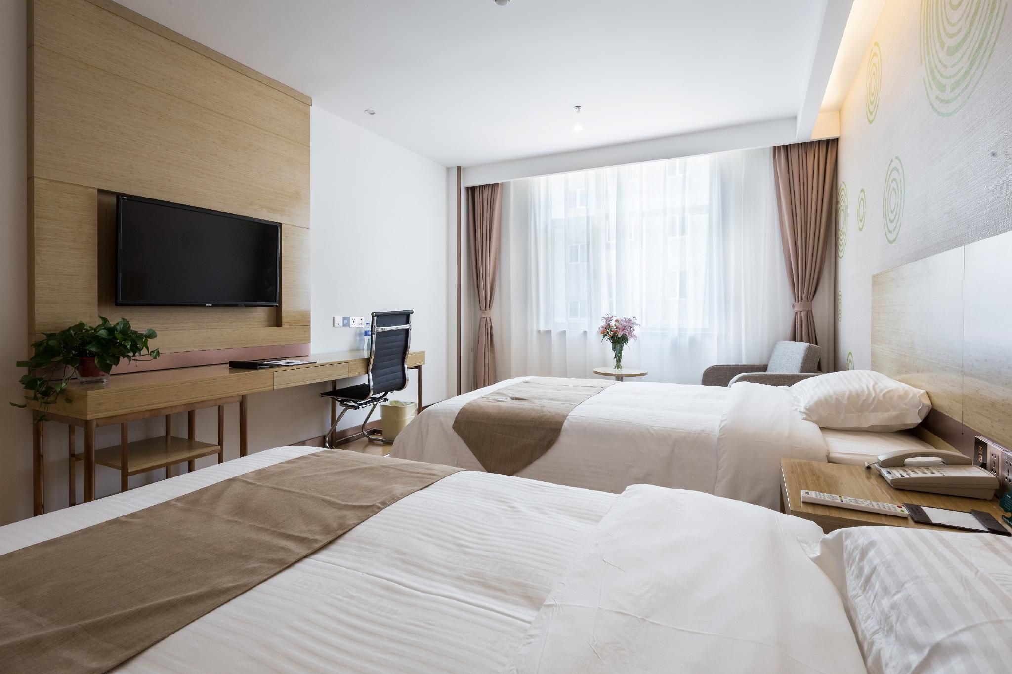 A hotel room with two beds, a desk with a TV, a chair, a small table with a vase, and a window with curtains.