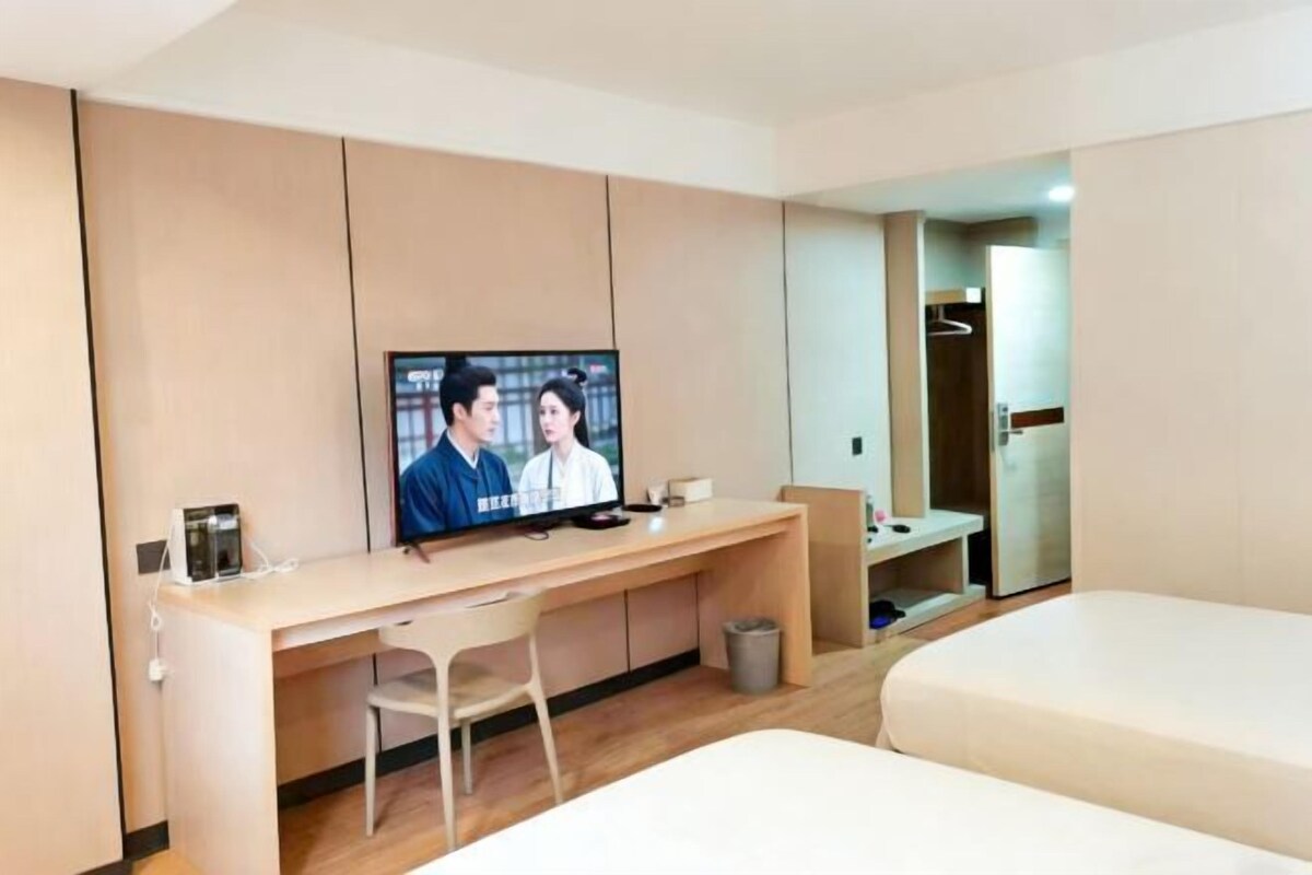 Una habitación de hotel con cama, escritorio, silla, televisor y espejo.