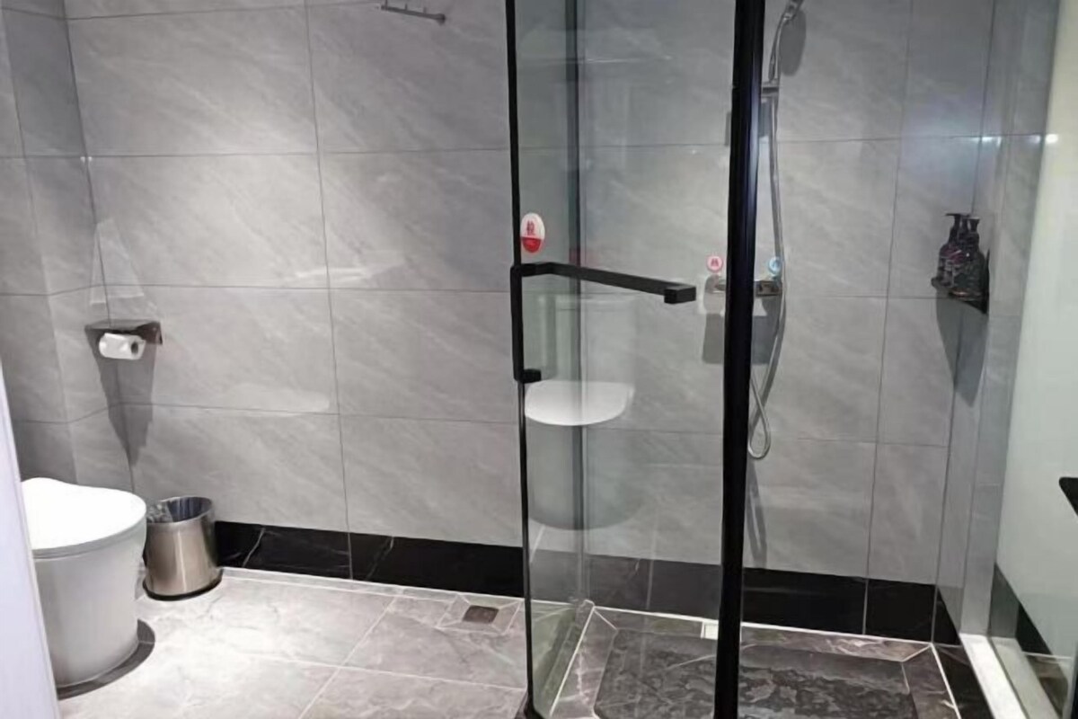 Un baño moderno con ducha de vidrio, inodoro y cubo de basura.