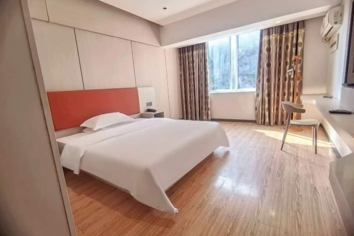 Hotellihuone, jossa on sänky, työpöytä, tuoli, ikkuna verhoilla ja seinälle asennettu ilmastointilaite.
