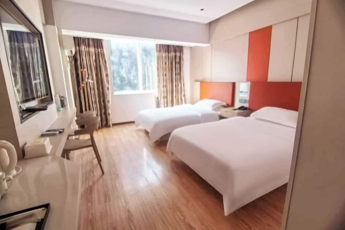 Hotellihuone, jossa on kaksi sänkyä, työpöytä tuolilla, televisio ja ikkuna, jossa on verhot.