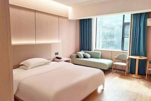 Quarto de hotel com uma cama grande, um sofá, uma mesa pequena e uma janela com cortinas.