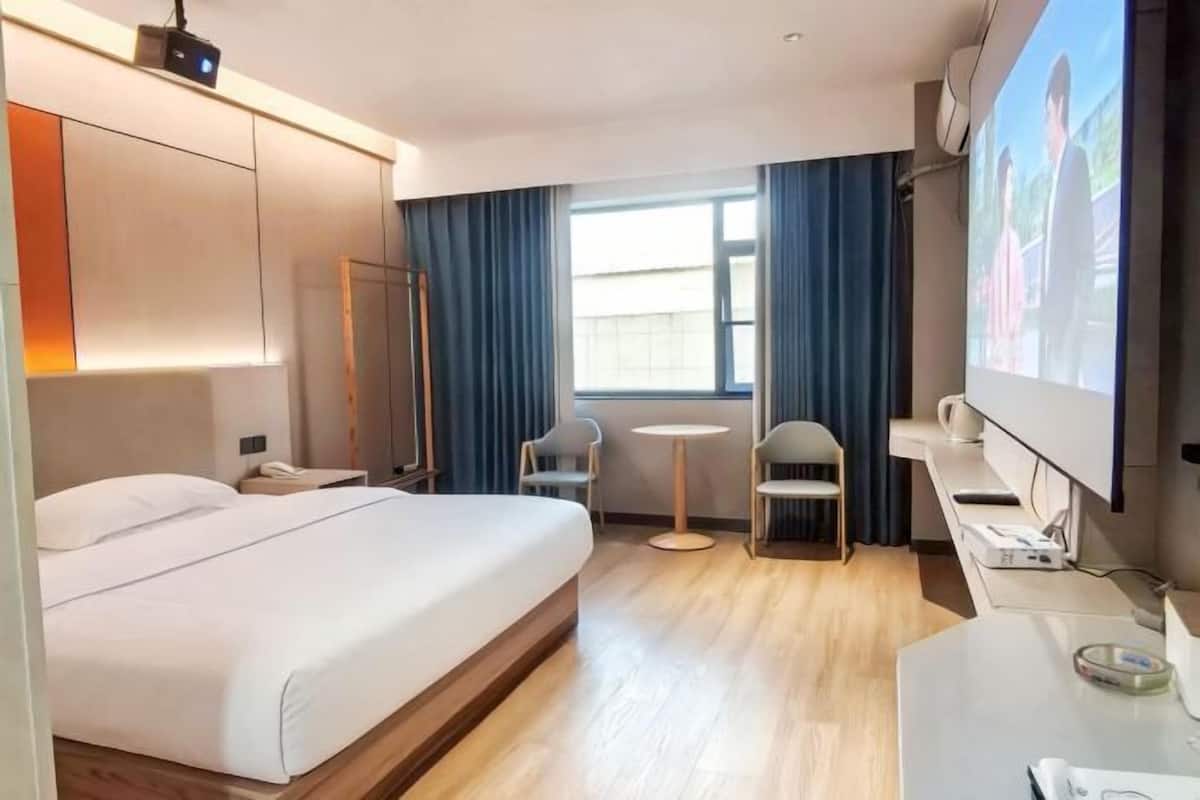 Hotellihuone, jossa on sänky, työpöytä, tuoli, televisio ja ikkuna, jossa on verhot.