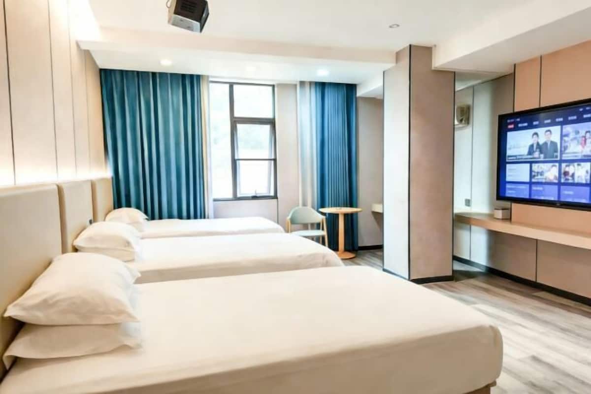 Hotellihuone, jossa on kaksi sänkyä, televisio, työpöytä ja ikkuna, jossa on verhot.