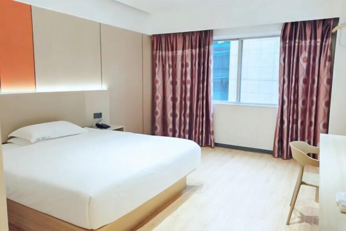 A hotel room with a bed, a desk, and a window with curtains.