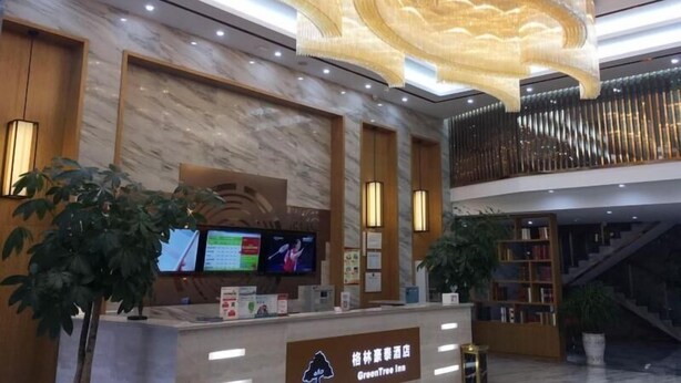 A hotel reception area with a marble wall, a reception desk, a large TV screen, and a staircase leading to an upper level. - Greentree Inn Yingtan Xinjiang New District Munici (Yingtan)